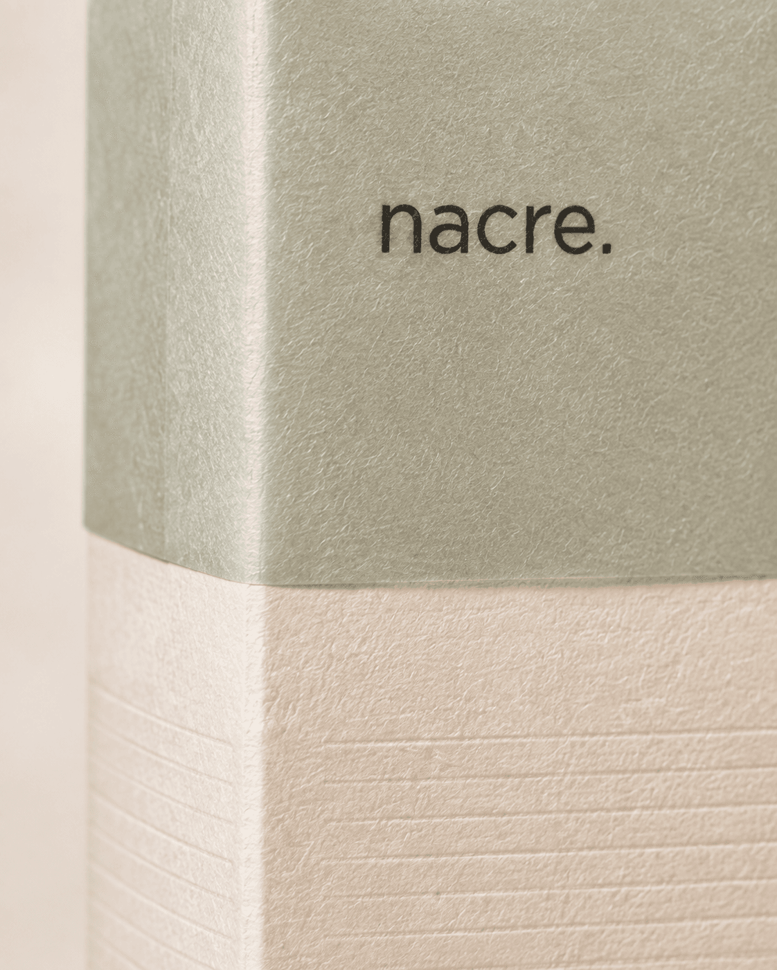 Detalle macro de la capa de papel glassine verde mineral de NACRE encontrándose con el papel marfil texturado.