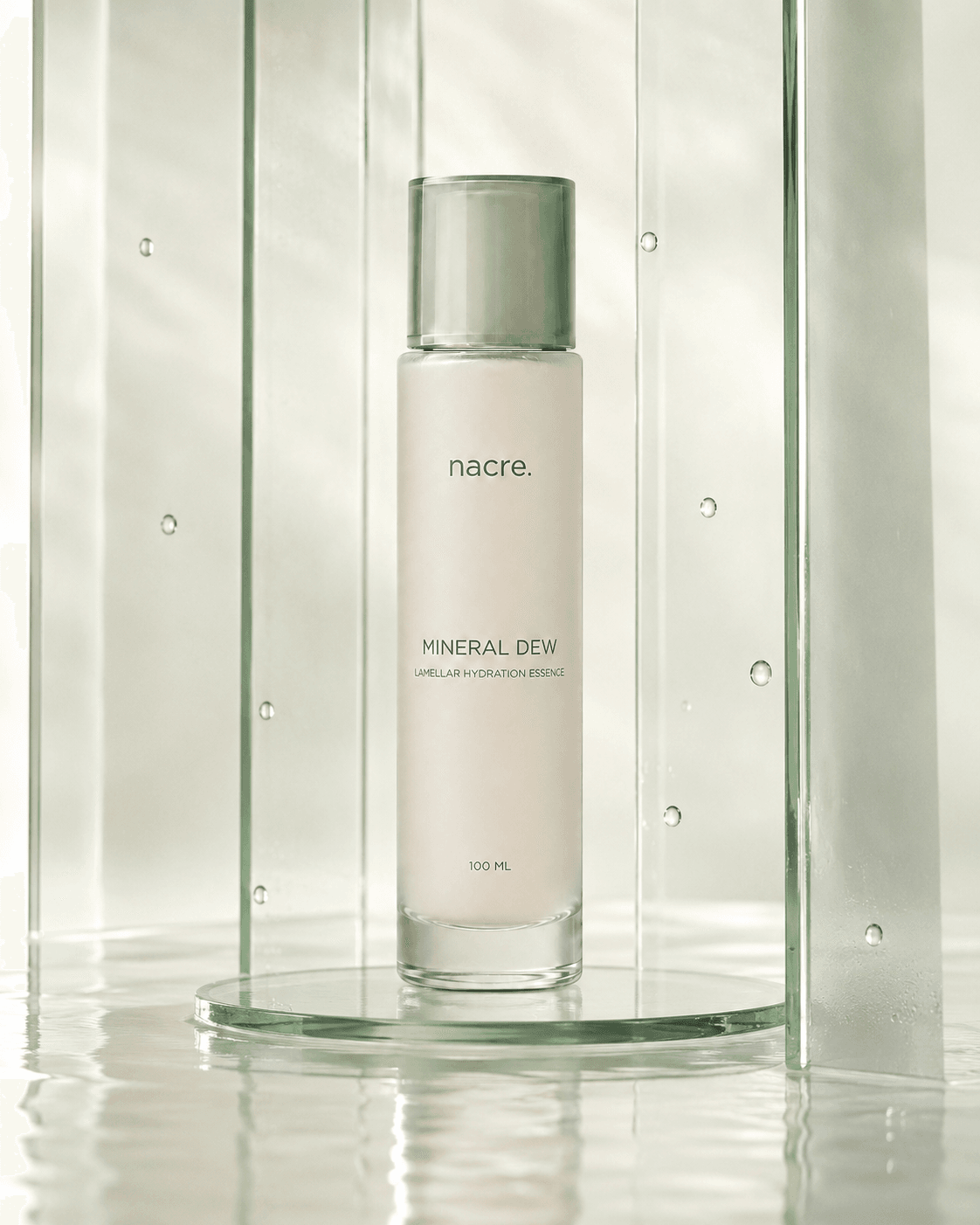 Esencia NACRE Mineral Dew enmarcada por paneles de vidrio verticales y gotas suspendidas.